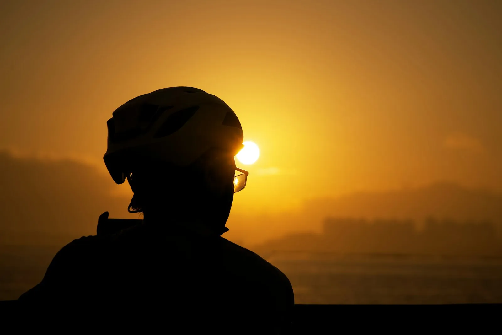 Silhouette of a worker in a hard hat against a setting sun