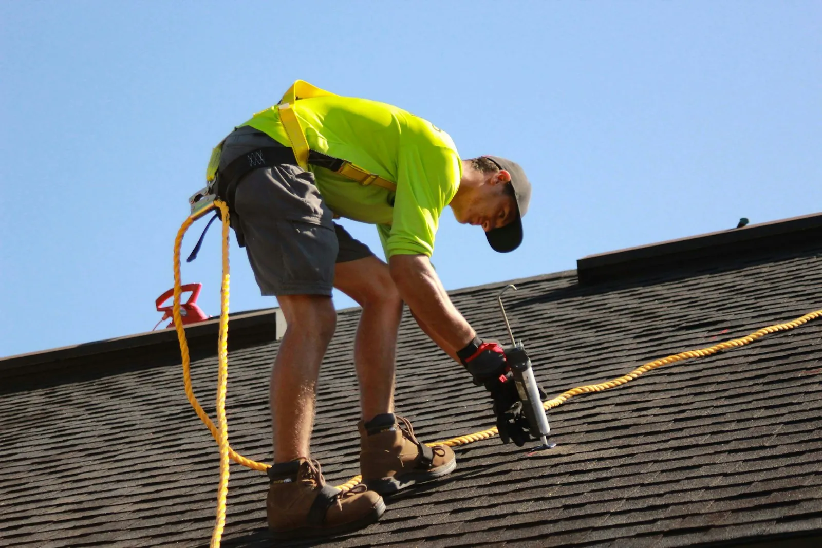 Roofer in a safety harness working on a shingle roof under a blue sky